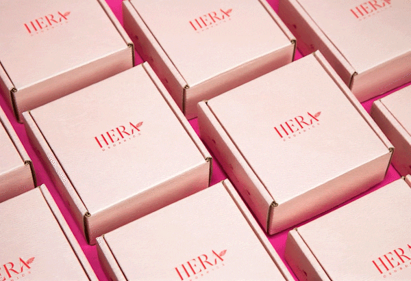 Campaign photography for Hera Organics showing branded product packaging arranged in a geometric pattern on a pink background